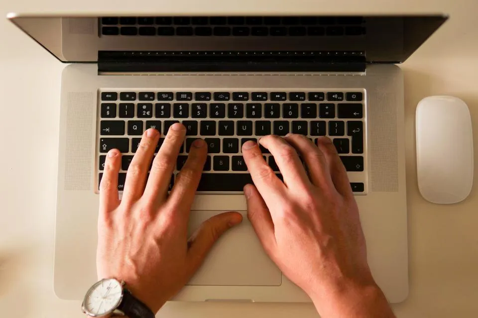 มองจากด้านบน มือพิมพ์คีย์บอร์ดโน้ตบุ๊ค MacBook สีเงินบนโต๊ะ