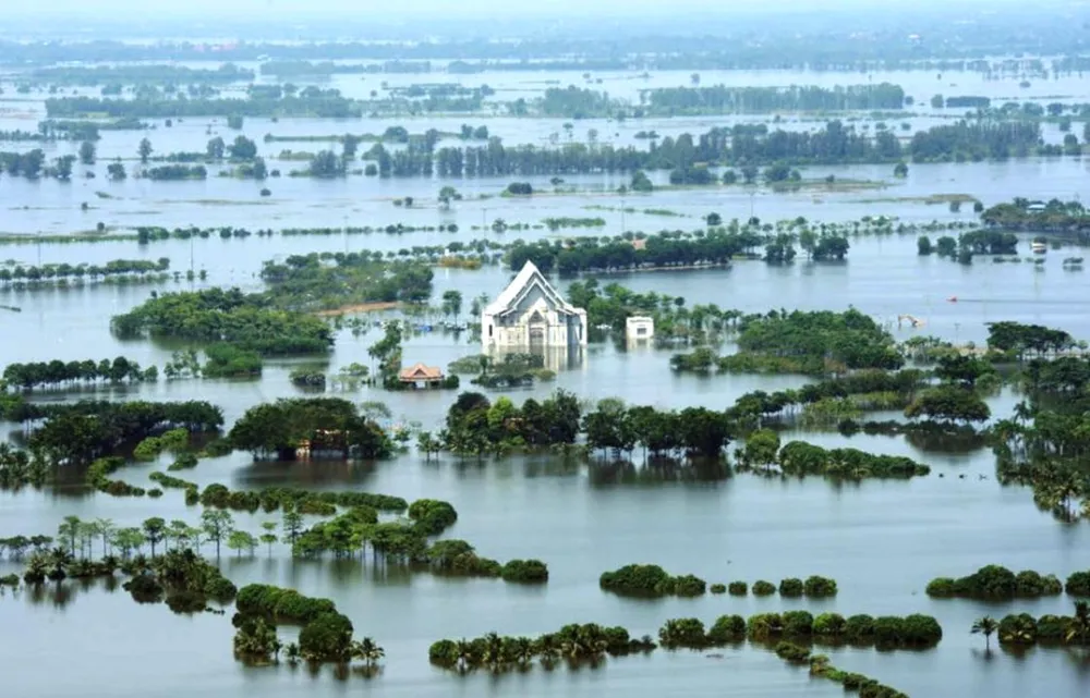 ภาพมุมสูงของบ้านและวัดที่จมอยู่ใต้น้ำท่วมในพื้นที่ภาคกลางของไทย ปี 2554 เห็นเพียงหลังคาและยอดต้นไม้พ้นน้ำ