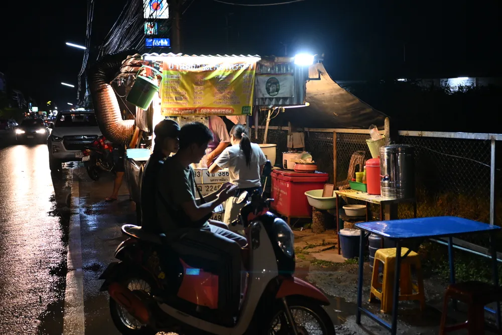 มอเตอร์ไซค์จอดอยู่ที่ร้านอาหารข้างทางบนถนนเปียกฝนตอนกลางคืนในเมืองไทย