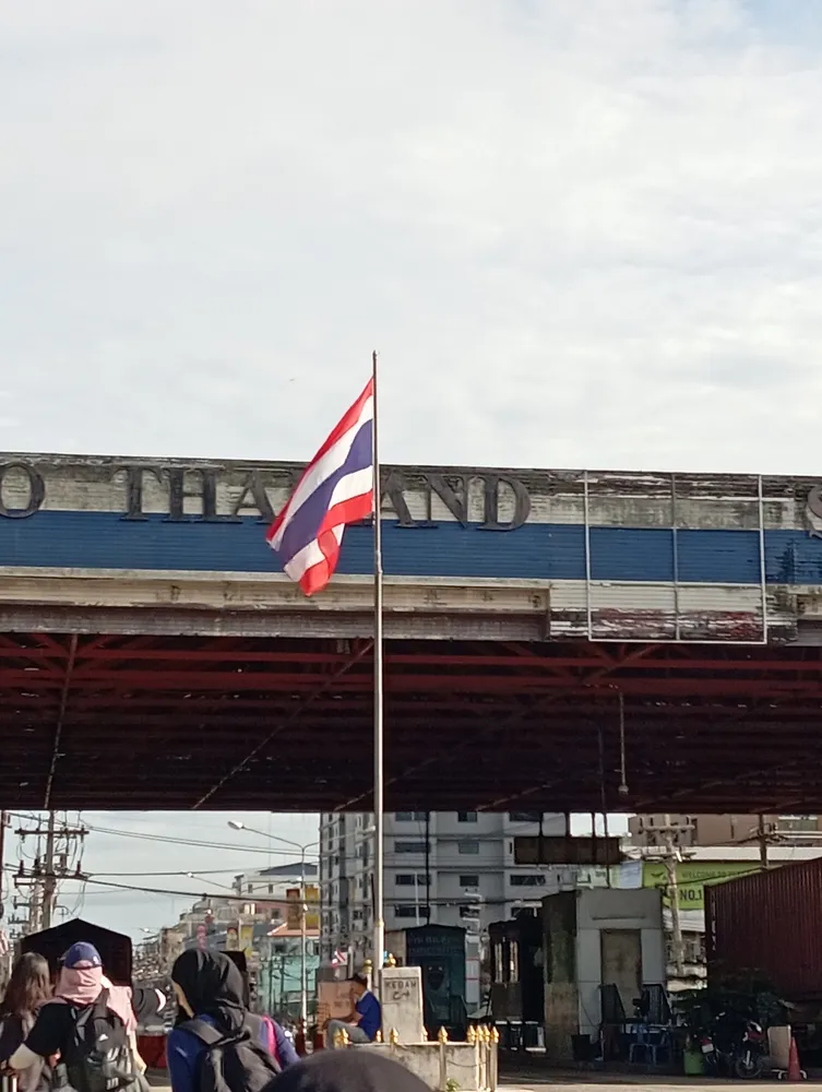 ประตูทางเข้าด่านสะเดา พร้อมธงชาติไทยและป้าย "TO THAILAND" — Song GK, CC BY 4.0 (Wikimedia Commons)